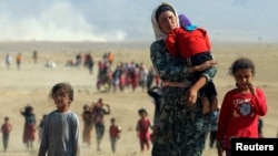 FILE - Displaced people from the minority Yazidi sect, fleeing violence from forces loyal to the Islamic State in Sinjar town, walk towards the Syrian border on the outskirts of Sinjar mountain near the border town of Elierbeh, Aug. 11, 2014.