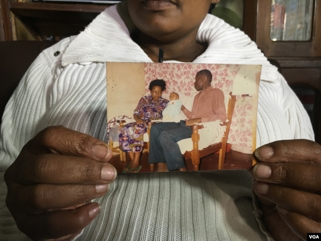 Pamela Olum holds up a picture of herself with her husband and their first-born child. Lawrence Olum was one of the 213 who died in the 1998 bomb attack in Nairobi, Kenya. (M. Yusuf/VOA)