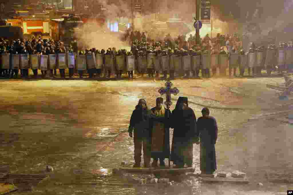 Các giáo sĩ Chính Thống giáo đứng cầu nguyện trong thủ đô Kyiv, giữa một bên là người biểu tình ủng hộ hội nhập EU và bên kia là cảnh sát, 24/1/14