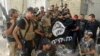 FILE - Iraqi security forces backed by Shiite and Sunni pro-government fighters celebrate as they hold a flag of the Islamic State militant group they captured in Ramadi, Anbar province, Iraq, July 26, 2015.