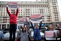 FILE - Russians hold placards during a protest against plans to raise the retirement age and reform the current pension system, in front of the Russian State Duma, the lower house of the Russian Parliament, in Moscow, Russia, July 19, 2018.