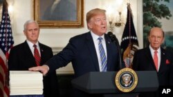 FILE - President Donald Trump reaches to touch a copy of the $1.3 trillion spending bill as he speaks in the Diplomatic Room of the White House in Washington, March 23, 2018.