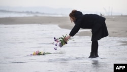 A woman puts flowers into the sea to pray for victims of the 2011 earthquake and tsunami in Sendai, northern Japan, March 11, 2016. 