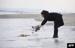 FILE - A woman puts flowers into the sea to pray for victims of the 2011 earthquake and tsunami in Sendai, northern Japan, March 11, 2016.