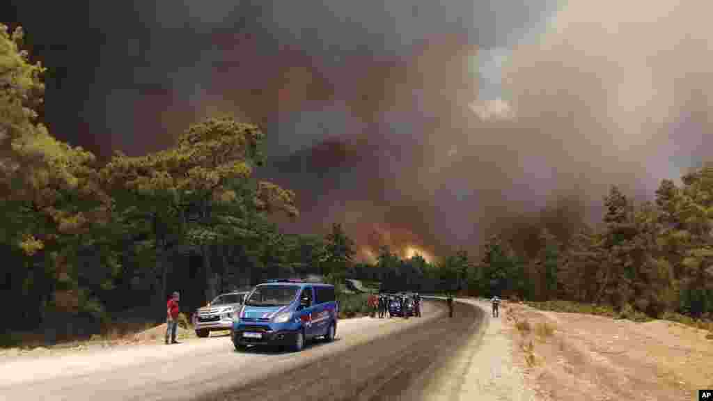 Paramilitary police officers and people watch as a wildfire fanned by strong winds rage near the Mediterranean coastal town of Manavgat, Antalya, Turkey.