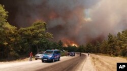 Paramilitary police officers and people watch as a wildfire strengthened by winds spread near the Mediterranean coastal town of Manavgat, Antalya, July 28, 2021. (AP Photo)