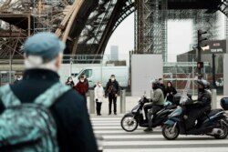 Pedestrians wear masks to prevent the spread of the COVID-19 as they wait at a crosswalk, near the Eiffel Tower, in Paris, Dec. 14, 2021.