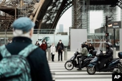 Pedestrians wear masks to prevent the spread of the COVID-19 as they wait at a crosswalk, near the Eiffel Tower, in Paris, Dec. 14, 2021.