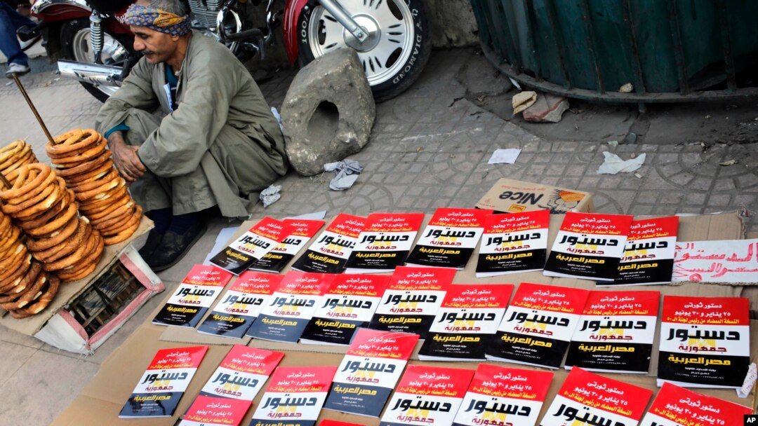 An Egyptian pritzel vender sits next to copies of the new constitution sold on a street in Cairo, Egypt, Saturday, Dec. 28, 2013.