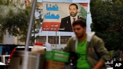 A street vendor stands in front of a poster of outgoing Prime Minister Saad Hariri that hangs on a street in Beirut, Lebanon, Nov. 6, 2017.