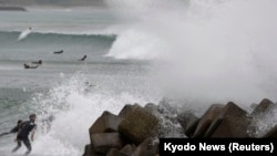 Waves crash as Typhoon Vongfong approaches Japan's main islands while surfers try to ride a wave at Eguchihama Beach in Hioki, Kagoshima prefecture, Oct. 12, 2014. 