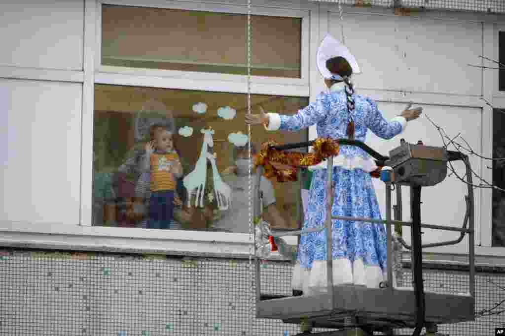 A young patient with relatives watches through a window as a Russian emergency rescue student dressed as Snegurochka (Snow Maiden) perform, outside the Morozov Children&#39;s City Clinical Hospital in Moscow.