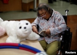 A resident reads a book during a session with 'AIBO'a pet dog robot and 'PARO' a robot seal at Shin-tomi nursing home in Tokyo, Japan, Feb. 2, 2018.