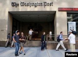 Seorang juru kamera televisi mengambil posisi ketika orang-orang berjalan di pintu masuk kantor pusat Washington Post di Washington, 5 Agustus 2013. (Foto: Reuters)
