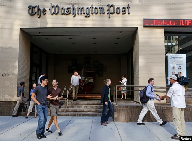 Seorang juru kamera televisi mengambil posisi ketika orang-orang berjalan di pintu masuk kantor pusat Washington Post di Washington, 5 Agustus 2013. (Foto: Reuters)