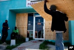 Trabajadores en Freeport, Bahamas, cubren con madera el escaparate de una tienda mientras se preparan para la llegada del huracán Dorian, el viernes 30 de agosto de 2019. AP.