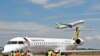 L’équipage au sol prépare un avion Bombadier d’Ouganda Airlines pour le départ, un avion exploité par Ethiopian Airlines décollant en arrière-plan à l’aéroport d’Entebbe lors du lancement du vol inaugural de Uganda Airline vers l’aéroport international Jo