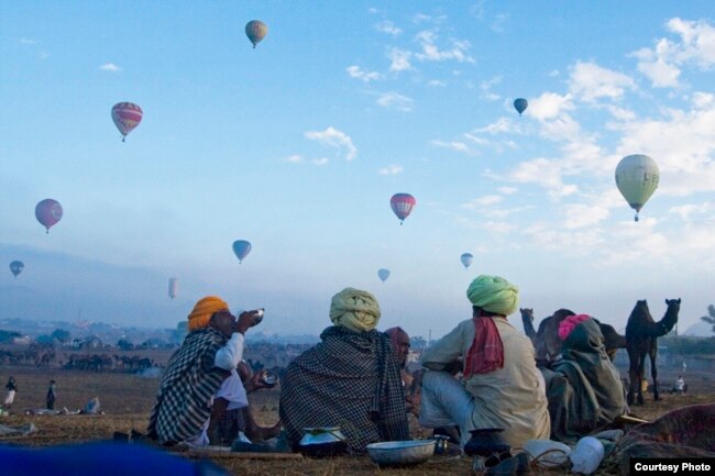 The camel traders were engaged in breakfast while the blue sky was decorated with the balloons.