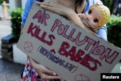 Seorang aktivis membawa boneka dan poster bertuliskan "polusi udara membunuh bayi" di luar gedung Pengadilan Negeri Jakarta Pusat saat sidang gugatan class action terkait polusi udara, 16 September 2021. (Foto: Willy Kurniawan/Reuters)