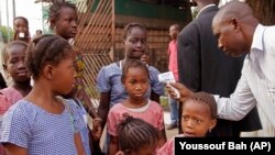 FILE - A health care worker, right, takes the temperatures of school children for signs of the Ebola virus before they enter their school in the city of Conakry, Guinea, Jan. 19, 2015. 