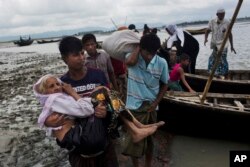 A Rohingya ethnic minority from Myanmar carries an elderly woman as they alight from a local boat on which they crossed a river, after crossing over to the Bangladesh side of the border near Cox's Bazar's Dakhinpara area, Sept. 2, 2017.
