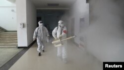 Dos voluntarios desinfectan un complejo residencial en la ciudad china de Wuhan, considerada como el epicentro del brote del coronavirus, el 22 de febrero de 2020.