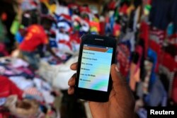 FILE - A man holds up his mobile phone showing an M-Pesa mobile money transaction page at an open-air market in Kibera in Kenya's capital, Nairobi, Dec. 31, 2014.