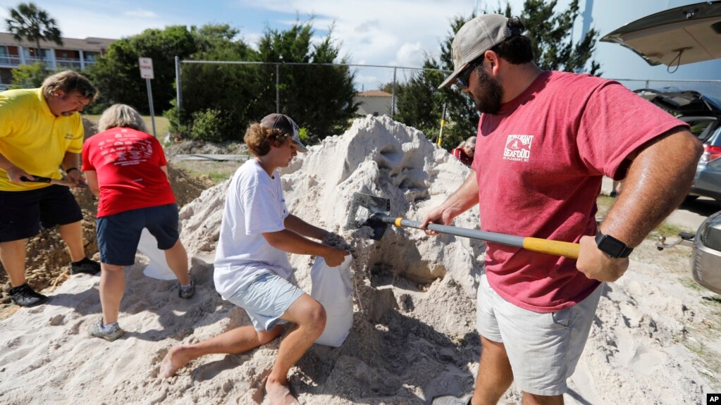 Walker Townsend (derecha), de Isle of Palms, Carolina del Sur, llena un saco de arena que sostiene Dalton Trout, en un estacionamiento municipal donde se reparte arena de forma gratuita dentro de los preparativos para la llegada del huracán Florence a la región, el 10 de septiembre de 2018. (AP Foto/Mic Smith)