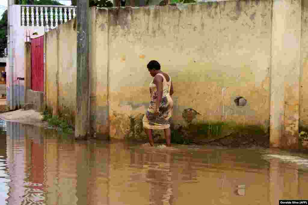Uma moradora caminha pela &#225;gua nas ruas inundadas do Futungo, Luanda - Angola, a 20 de Abril, depois das fortes chuvas de dia 19