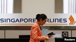 FILE - A staff member walks by a Singapore Airlines (SIA) logo at a ticketing counter at Changi airport in Singapore.