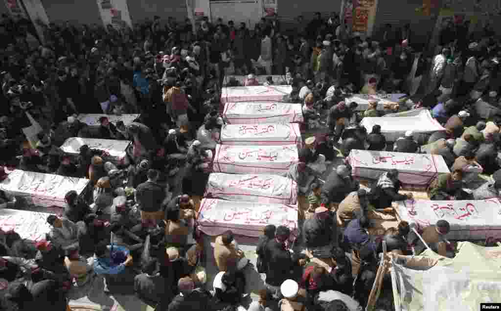 Shi'ite Muslims sit beside the covered bodies of victims who were killed in Tuesday's bomb attack on a bus, during a protest in Quetta, Jan. 22, 2014.