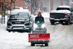 A worker drives a sidewalk snow plow down the middle of a street in Pittsburgh, Pennsylvania, Jan. 17, 2022.