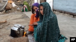 FILE - Internally displaced girls warm up by a stove after their family left their village in the Achin district of Afghanistan, due to clashes between the Islamic State group and other insurgent groups. 