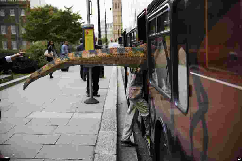 The tail of a dinosaur costume sticks out as the person wearing it boards a bus near the Houses of Parliament in London.
