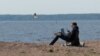 Seorang pria bekerja dengan menggunakan smartphone dan laptopnya, sambil duduk di pantai Teluk Finlandia di tengah pandemi Covid-19 di Saint Petersburg, Rusia, 27 Mei 2020. (REUTERS / Anton Vaganov)