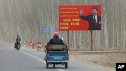 FILE - China's Xi Jinping is seen on a billboard with the slogan, "Administer Xinjiang according to law, unite and stabilize the territory, culturally moisturize the territory, enrich the people and rejuvenate the territory," in Xinjiang Uyghur Autonomous Region, March 21, 2021. 