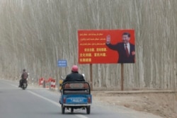 FILE - Chinese President Xi Jinping is seen on a billboard with the slogan, "Administer Xinjiang according to law, unite and stabilize the territory, culturally moisturize the territory, enrich the people and rejuvenate the territory, and build the territory for a long term," in Yarkent County in Xinjiang, March 21, 2021.