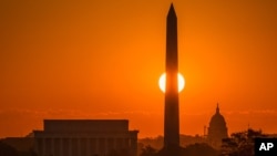 The rising sun passes behind on the Washington Monument early in the morning, Sept. 14, 2016, in Washington on what is expected to be another 90 degree day in the Nation's Capitol. 