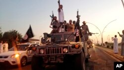 FILE - Fighters from the Islamic State group parade in a commandeered Iraqi security forces armored vehicle down a main road at the northern city of Mosul, Iraq, June 23, 2014.