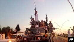 FILE - Fighters from the Islamic State group parade in a commandeered Iraqi security forces armored vehicle down a main road at the northern city of Mosul, Iraq.