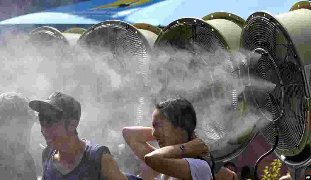 Tennis fans stand before cool water mist to cool down at the Australian Open tennis championship in Melbourne, Australia.