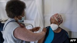 FILE: An health care worker administers a jab containing Pfizer vaccine on a caregiver. (Photo by Michele Spatari / AFP)