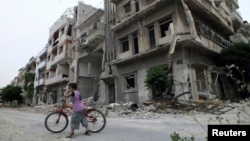 A boy rides a bicycle in front of damaged buildings in Homs, Syria, May 24, 2013. 