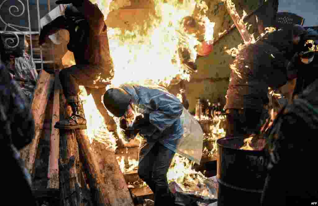 Protesters burn as they stand behind burning barricades during clashes with police in Kyiv. Ukraine&#39;s embattled leader announced a &quot;truce&quot; with the opposition as he prepared to get grilled by visiting EU diplomats over clashes that killed 26 and left the government facing diplomatic isolation.