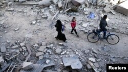 People walk on the rubble of damaged buildings at a site hit yesterday by airstrikes in the rebel held Douma neighborhood of Damascus, Syria, Nov. 18, 2016.