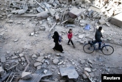 FILE - People walk on the rubble of damaged buildings at a site hit by airstrikes in the rebel-held Douma neighborhood of Damascus, Syria, Nov. 18, 2016.