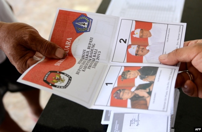 Seorang petugas TPS memberikan surat suara di TPS di Kuta, Bali, saat pelaksanaan pilkada, 9 Desember 2015. (Foto: AFP)