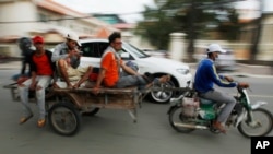 A Cambodian worker, third from left, views his mobile phone on a motor cart forwarding to work, in Phnom Penh, Cambodia, Tuesday, Aug. 11, 2015. Mobile phones are more popular than desktop computers in Cambodia. (AP Photo/Heng Sinith)