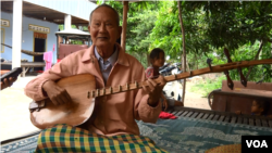 Sitting on a wooden bed in Tropeang Kok village, Takeo province, Brach Chhoun uses both hands, full of wrinkles, to play. 