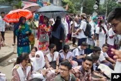 Bangladeshi students block a road during a protest, as their guardians stand nearby holding umbrellas, in Dhaka, Bangladesh, Saturday, Aug. 4, 2018.